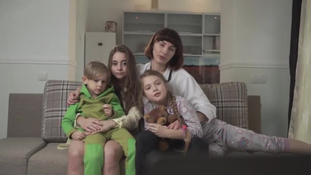 Family sitting on the couch in the guest room and watching TV expressive and emotionally. Older sisters and younger siblings spend time together. Family holiday. — Stock video