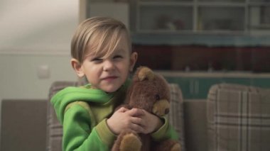 Oturma odasında kanepede yanında bir oyuncak ayı durduğunu sarılma pijama küçük şirin komik çocuk portresi. Mutlu neşeli bir çocuk. Ağır çekim.