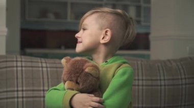 Bir küçük güleryüzlü neşeli yakışıklı bir oyuncak ayı ayakta oturma odasında sarılma pijama portresi. Mutlu neşeli bir çocuk. Ağır çekim.