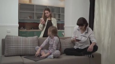 İki büyük kız Mesaj ayarlarý, cep telefonları daha genç bir kız evde kanepede otururken dizüstü bilgisayarda yazarak. Küçük kız yakın laptop ve aileden dikkatini çekmek çalışıyor
