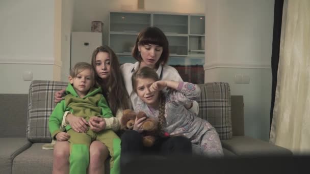 Rodina sedí na gauči v pokoji pro hosty a emocionálně sledování televize. Starší sestry a mladší děti trávit čas společně. Rodinná dovolená. — Stock video