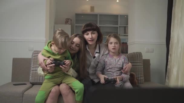 Irmãs mais velhas felizes e crianças mais novas alegres sentadas no sofá jogando videogames no quarto de hóspedes. Férias familiares divertidas . — Vídeo de Stock