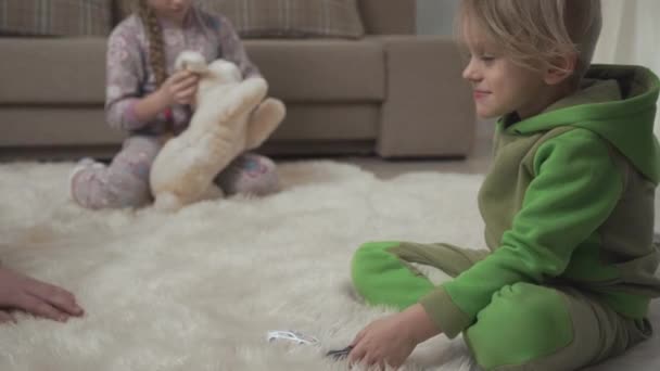 Deux enfants mignons allongés sur le tapis moelleux sur le sol en jouant avec des jouets à la maison. Main masculine touchant le nez d'un enfant joyeux. Bon week-end enfants . — Video