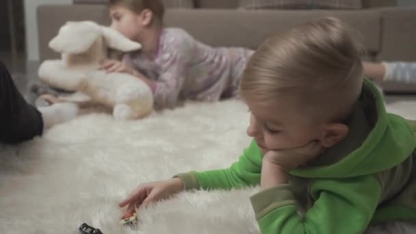 Duas crianças fofas deitadas no tapete fofo brincando com brinquedos no chão. Crianças felizes fim de semana . — Vídeo de Stock