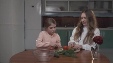 Küçük kız kardeşi yardımcı olur ablası rahat mutfakta küçük bir masada oturup kahvaltı için coocking sebze salatası.