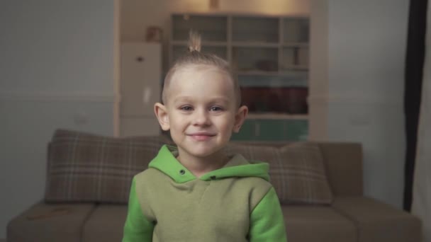 Portrait de petit garçon avec une coupe de cheveux élégante debout sur le fond du canapé à la maison . — Video