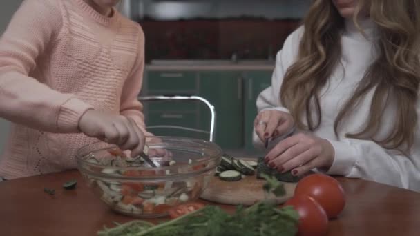 Irmã mais nova ajuda a irmã mais velha coocking salada de legumes para o café da manhã sentado em uma pequena mesa na cozinha acolhedora. Relação irmãs . — Vídeo de Stock