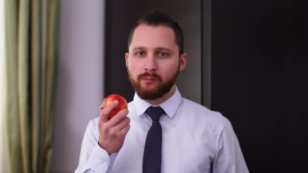 Retrato de un exitoso hombre de negocios barbudo con una camisa con corbata comiendo una manzana. Concepto de un estilo de vida saludable . — Vídeo de stock