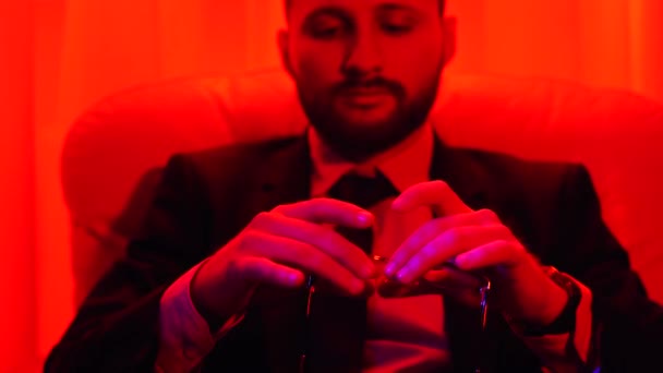 Portrét vousatého úspěšný podnikatel oblečený v obleku, kroucení brýle sedí v jasném světle červená. — Stock video
