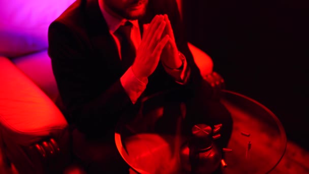 Un hombre sentado en la mesa con cinco cajas de balas. Disparos en luz roja brillante — Vídeos de Stock