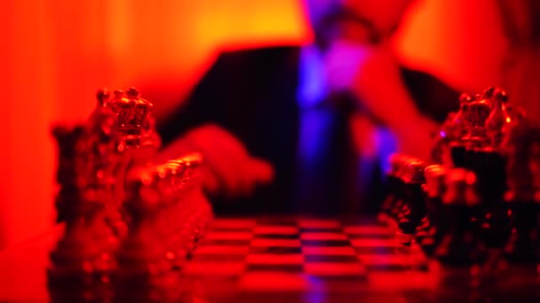 背景をぼかした写真の上に座ってビジネス スーツを着た男は、チェスを果たしています。明るい赤色光での撮影. — ストック動画