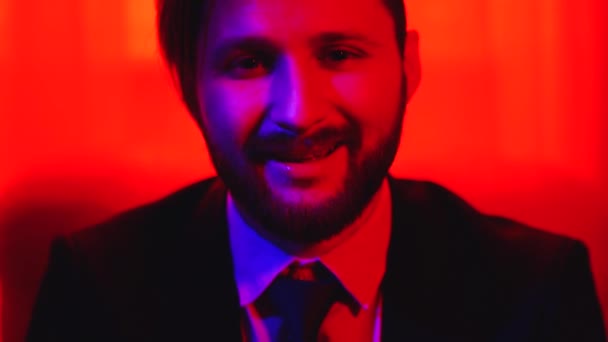 Retrato del hombre barbudo sonriente mirando a la cámara aislada sobre fondo de luz roja brillante . — Vídeos de Stock