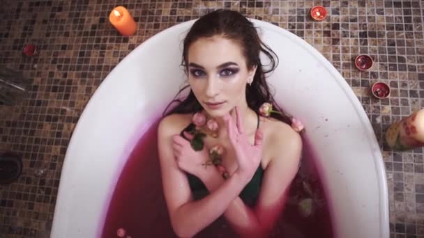 Jonge vrouw met lichte make-up nemen van een bad in de camera kijken. Meisje ontspannen in de badkamer met het branden van kaarsen — Stockvideo