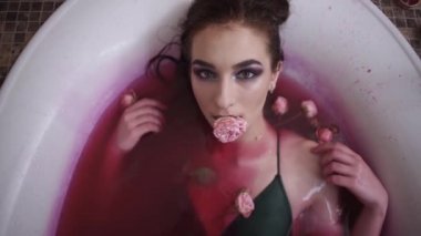 Çiçekli banyo ağzına gül tutan genç kadın portresi kapatın. Bayan kamera arıyorum. Sevimli güzel kız rahatlatıcı banyo. Ağır çekim.