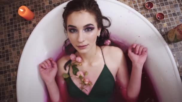 Mujer bastante tierna con maquillaje brillante tomando un baño con rosas. Chica relajante en el baño con velas encendidas. Movimiento lento . — Vídeos de Stock