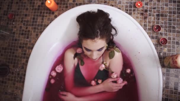 Молодая женщина с ярким макияжем принимает ванну с розами. Стрельба сверху, вид сверху. Медленное движение . — стоковое видео