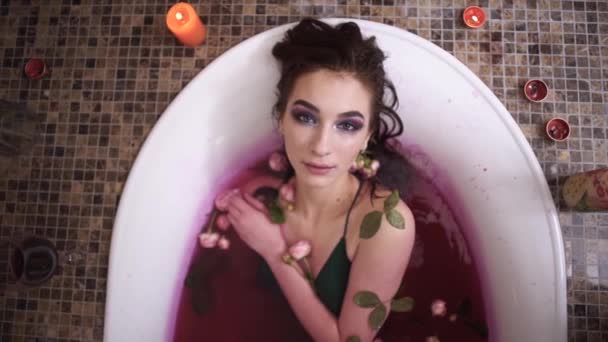 Mulher jovem sensual bonito relaxante tomando banho com rosas no salão de spa. Menina desfrutando no banheiro com velas acesas — Vídeo de Stock