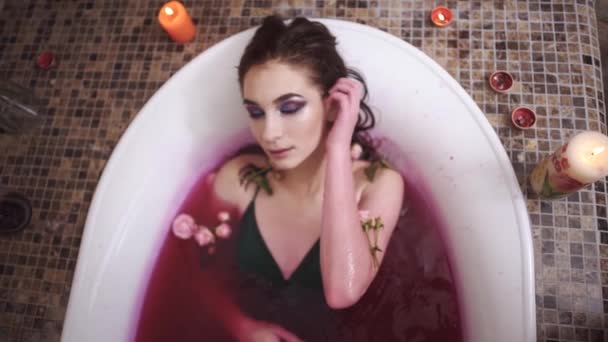 Mooie tedere sensuele vrouw met lichte make-up ontspannend nemen bad met rozen in spa salon. Schattige dame genieten in de badkamer met het branden van kaarsen — Stockvideo