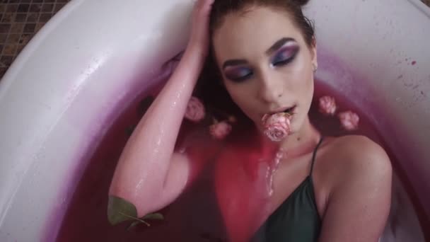 Porträtt av sensuell kvinna med ros i munnen tar ett bad i spa. Vacker flicka att släppa en ros från hennes mun avkopplande i badrummet. Flyttar kameran bort och flickan går ur fokus. Slow motion — Stockvideo