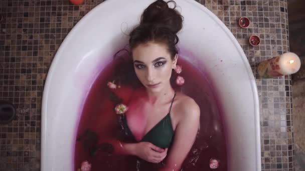 Retrato de mujer joven bastante tierna con brillante maquillaje relajante tomar un baño con rosas en el salón de spa. Linda chica disfrutando en el baño con velas encendidas. Movimiento lento . — Vídeo de stock