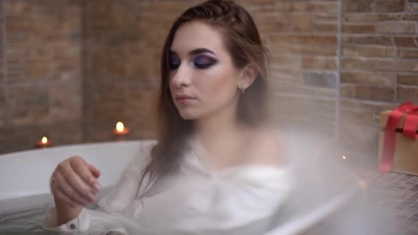 Portrait of beautiful woman in white shirt taking a bath. Cute girl enjoying in the bathroom with burning candles. — Stock Video