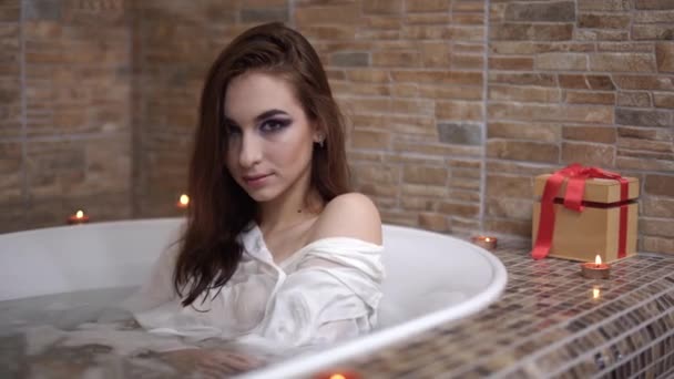 Vackra sensuella kvinnan i vit skjorta tar ett bad. Söt flicka njuter i badrummet med brinnande ljus. — Stockvideo