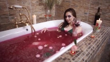 Parlak makyaj gül ile banyo olan kadın ve ve şarap içme. Yanan mumlar, şarap ve bir kase akvaryum akvaryum balığı ile banyoda zevk şehvetli kız.