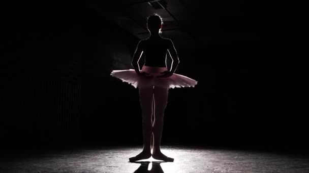 Молодая балерина, практикующая балет. Силуэт балерины выделен в центре внимания на черном фоне в студии. Женщина показывает классические балетные па. Медленное движение . — стоковое видео