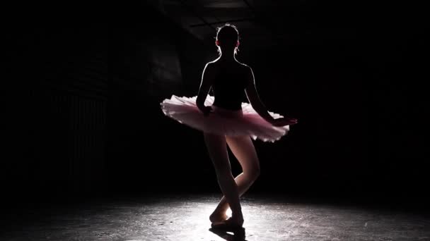 Beautiful silhouette of young ballerina on pointe shoes at black concrete floor background. Ballet practice. Beautiful slim figure of ballet dancer. Slow motion. — Stock Video