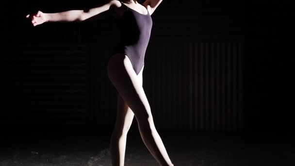 Bailarina flexible de pie sobre sus zapatillas de ballet puntiagudas en el centro de atención sobre fondo negro en el estudio. Movimiento lento . — Vídeo de stock