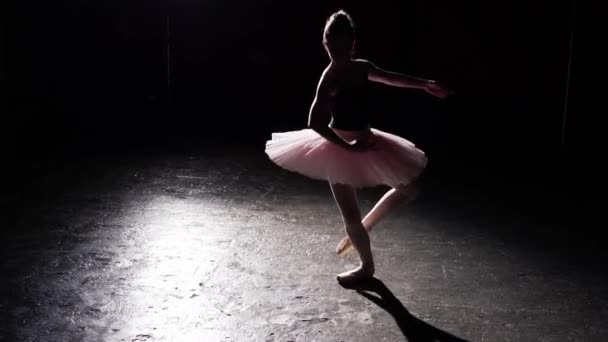 Profesionální elegantní flexibilní baletka tančí na její pointe baletní boty v pozornosti na černém pozadí ve studiu. Žena ukazuje klasický balet pas nosit tutu a pointe boty.