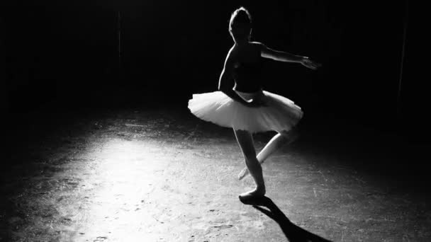 Профессиональная гибкая балерина танцует на пуантах балетных туфель в центре внимания на черном фоне в студии. Женщина показывает классические балетные па в пачках и пуантах. Черно-белый кадр . — стоковое видео