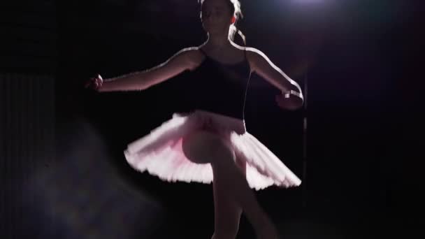 Flexibla flicka dansa på hennes pointe balettskor i rampljuset på svart bakgrund i studio. Professionella unga ballerina visar klassisk balett pas tutu och pointe skor. — Stockvideo