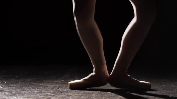 Изящная балерина танцует на пуантах балетных туфель в центре внимания на черном фоне в студии. Девушка показывает классические балетные па в пуантах. В кадре видны только женские ноги . — стоковое видео