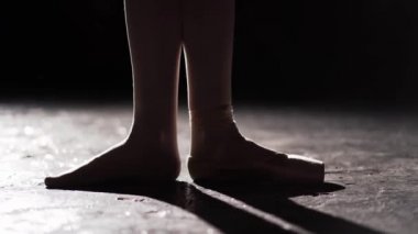 Spot Studio siyah arka plan üzerine ayak ayakta. Bir ayak diğer yalınayak bale ayakkabıları giyiyor. Portre.