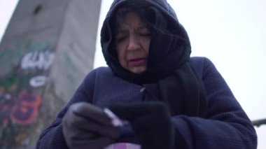 Ağlama ve hap alarak soğuk havalarda rüzgarlı gri köprüde ekose ile yetişkin evsiz kadın portre oturur