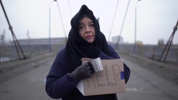 Portrét starého smutný žebrák pobytu na mostě v chladném větrném šedé počasí žádat o almužnu a pomoc — Stock video