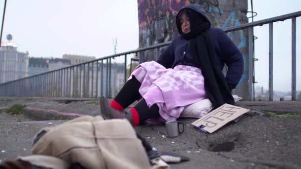 Erwachsene obdachlose Frau in kaltem windigem grauen Wetter, nachdem sie um Almosen und Hilfe gebeten hat, erhebt sich von dem Kissen, auf dem sie saß — Stockvideo