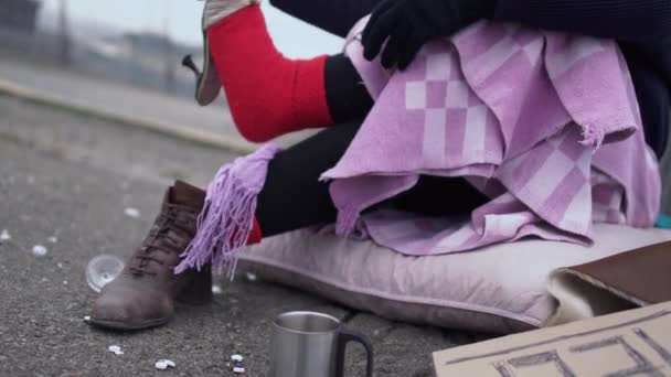 Obdachlose Frauen tragen Sandalen und ziehen Wollsocken an, während sie im Freien auf Pappe sitzen.