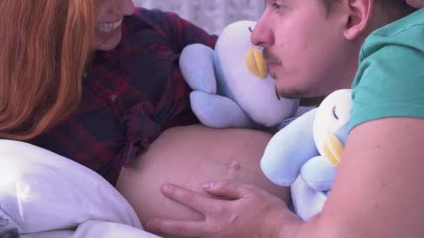 Papai beija e acaricia a barriga de sua esposa brincando com brinquedos suaves. Conceito de maternidade. Gravidez. Família feliz . — Vídeo de Stock