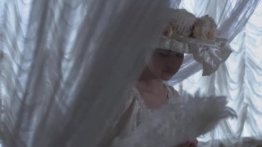 Şeffaf perdeler arka plan üzerinde duran ve tüy fan sallayarak topu cüppe ve beyaz şapkalı genç güzel kadın