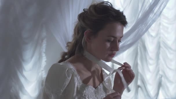 Jeune belle femme assise arround rideaux filet blanc et détache un ruban sur son cou — Video