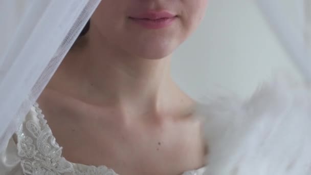 Молоді красиві губи і плечі жінки в білій весільній сукні, дівчина махає вентилятором пір'я на білому тлі на половині обличчя реальні люди серії — стокове відео