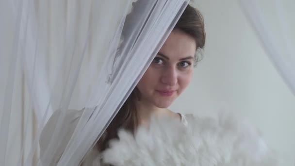 Портрет милої жінки, що махає білим вентилятором на білому тлі. Справжні люди серії. Ховаючись за завісою — стокове відео