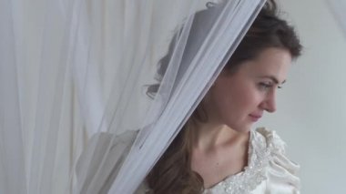 Beyaz Tüy fan sallayarak tül yakınındaki Genç Sevimli kadın. Kız giyim beyaz elbise ve güzel saç stili vardır. Gerçek insanlar serisi beyaz arka plan üzerinde. Perde arkasına saklanan