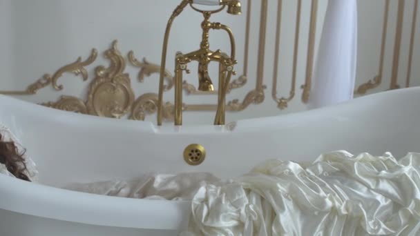 Молодая грустная женщина лежит в старомодной ванной в ванной, одетая в бальное платье крупным планом — стоковое видео