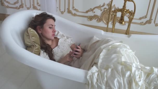 Giovane donna in abito bianco vintage sdraiato nello schermo ampty bagno toccando di presa di mano smartphone — Video Stock