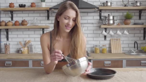 Retrato bonita mujer joven en lencería agitando un batidor en un tazón grande de pie en la cocina. Chica sensual cocinando en casa . — Vídeos de Stock