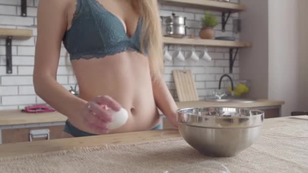 Mulher em lingerie com um belo torso quebra um ovo em uma tigela de pé na cozinha. Menina irreconhecível cozinhar em casa . — Vídeo de Stock
