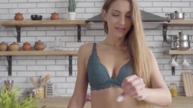 Portre sevimli genç kadın iç çamaşırı bir kasenin içine ve kamera un ve splash bir tutam alır. Gülümseyen kadın yarı giyinik rahat mutfakta yemek yapıyor. Eğlence genç güzel yalnız kadın.